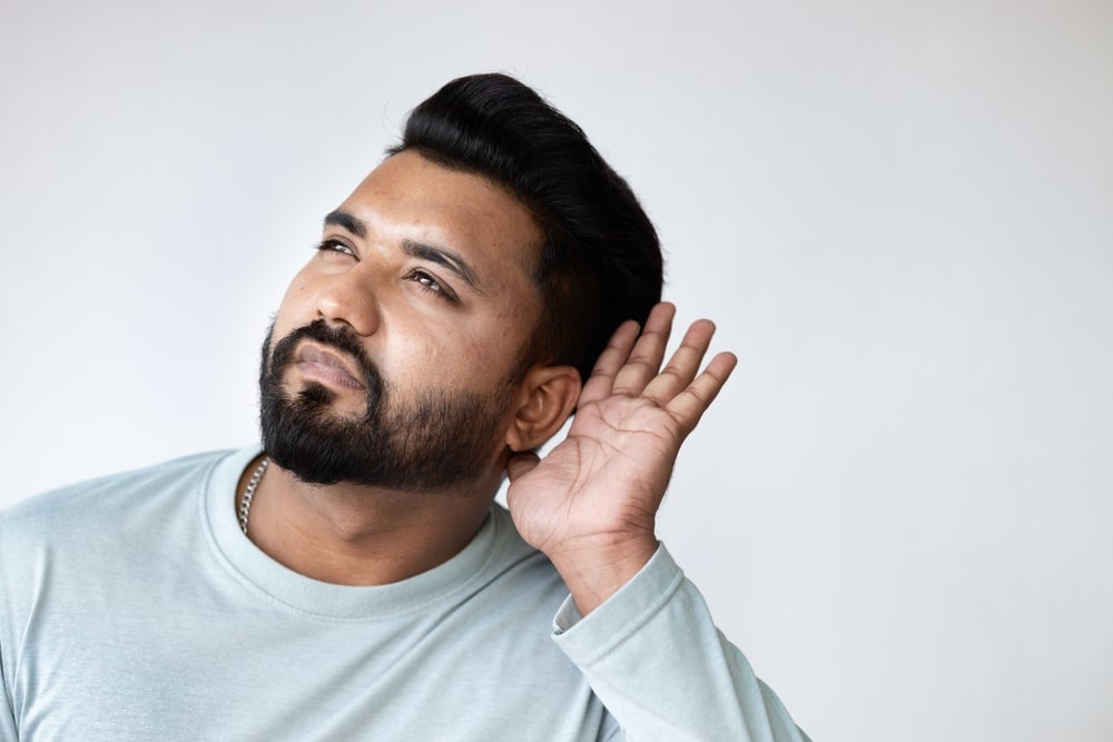 A man with hearing loss holding up his hand to his ear